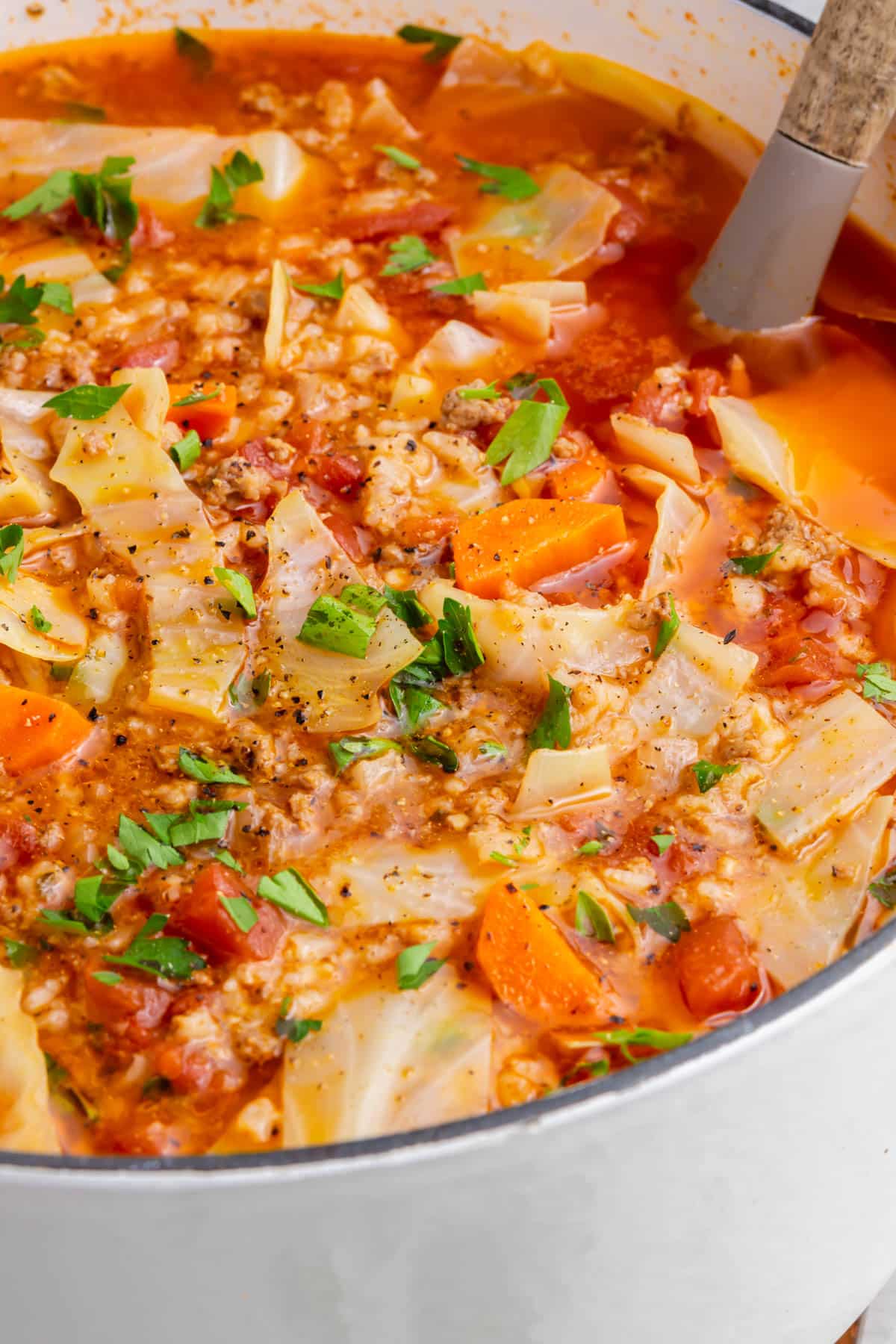 A dutch oven filled with cabbage roll soup with parsley and carrots with a spoon in it.