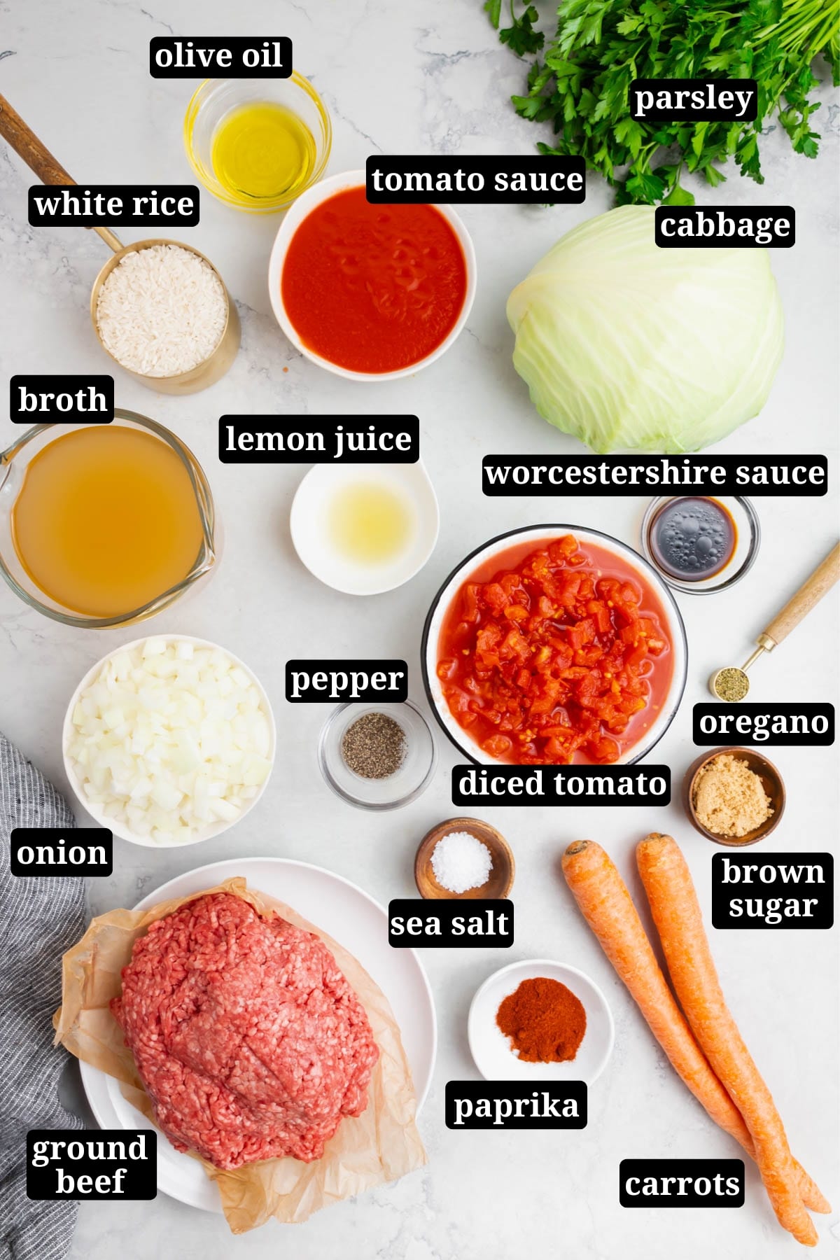 Ingredients in small bowls to make cabbage roll soup, including oil, tomato paste, rice, cabbage, chicken broth, worcestershire sauce, lemon juice, oregano, brown sugar, paprika, salt, pepper, onions, carrots and ground beef with text overlays over each ingredient.