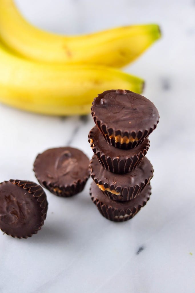 A stack of Chocolate Peanut Butter Banana Bites in front of a banana bunch.