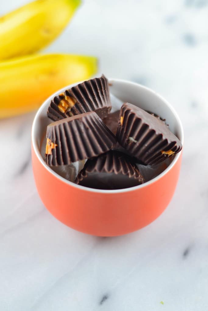 A bowl of chocolate peanut butter banana bites with whole bananas in the background.