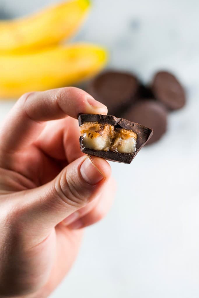 A hand holding a chocolate peanut butter banana bite that has been cut in half to see the inside.