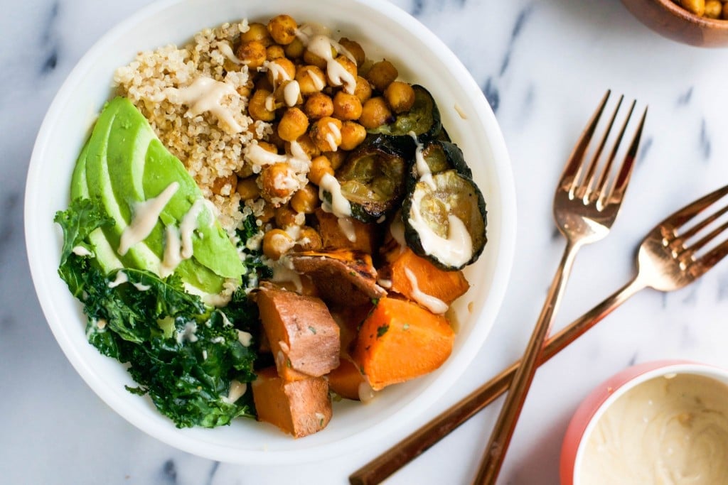 An overhead view of a quinoa bowl topped with chickpeas, sweet potatoes, kale, avocado, zucchini and creamy cashew sauce.