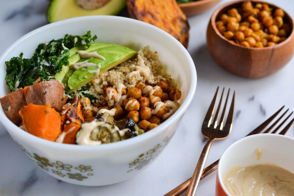 A bowl of quinoa, curried chickpeas, sweet potatos, avocado, zucchini, kale and a creamy cashew sauce.