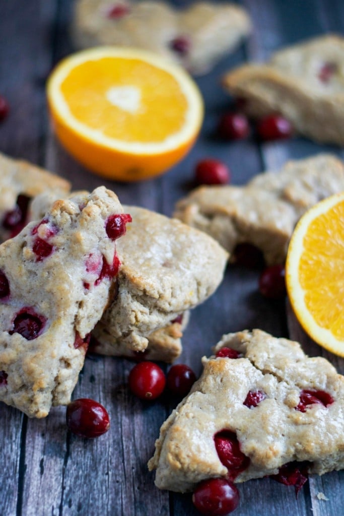 Vegan cranberry orange scones stacked on top of each other with orange halves on a wood table.