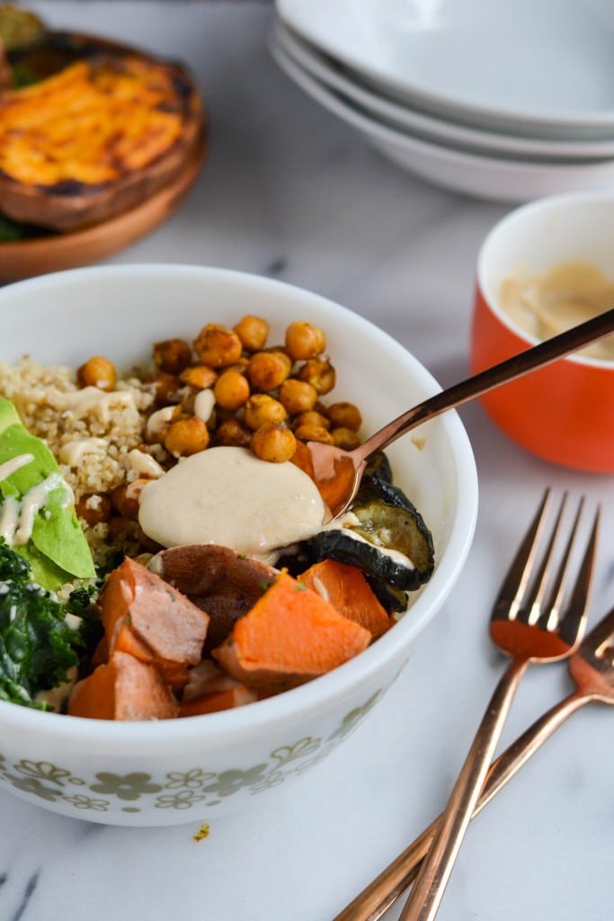 A spoon full of creamy cashew sauce being drizzled over a sweet potato chickpea quinoa bowl.