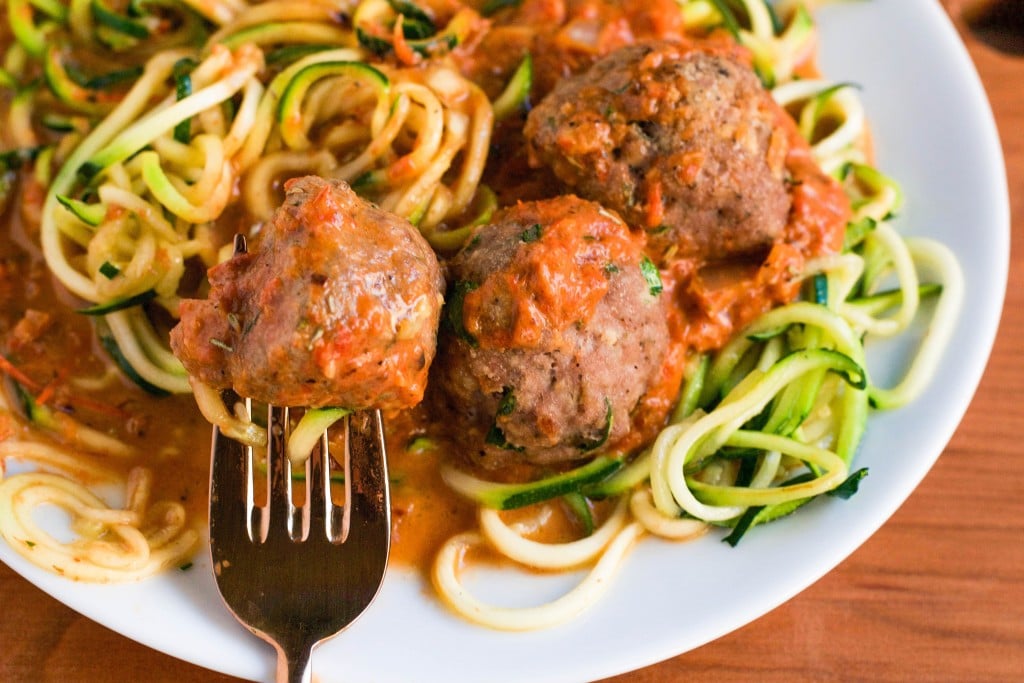 Zoodles with Turkey Meatballs in a Roasted Red Pepper Sauce with a fork sticking into the meatball