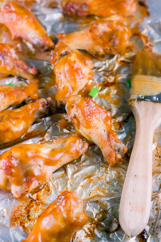 Mango habanero chicken wings on aluminum foil with a pastry brush.