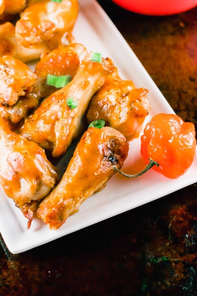 A platter of mango habanero chicken wings with habanero peppers on the side.