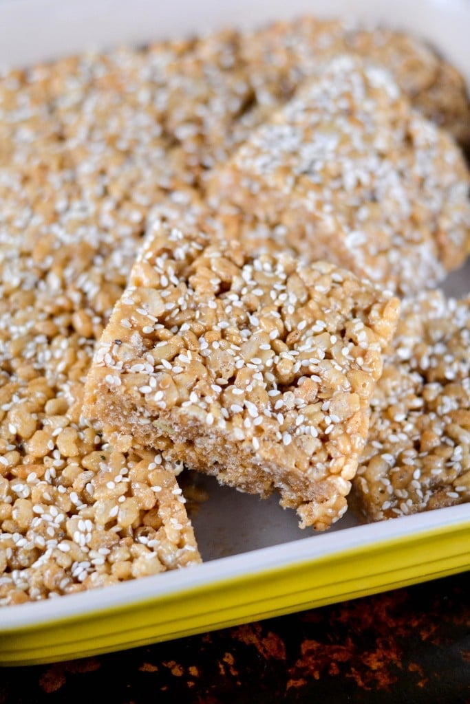 A baking dish with squares of tahini brown rice krispy treats topped with sesame seeds. 