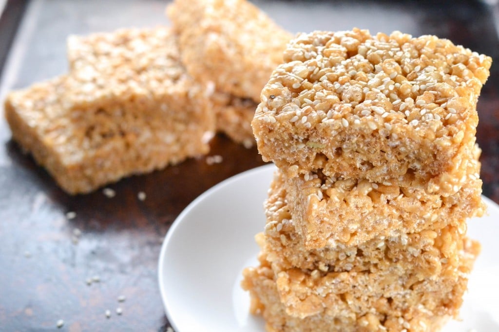 A stack of three tahini rice krispy treats on a white plate with more treats in the background.