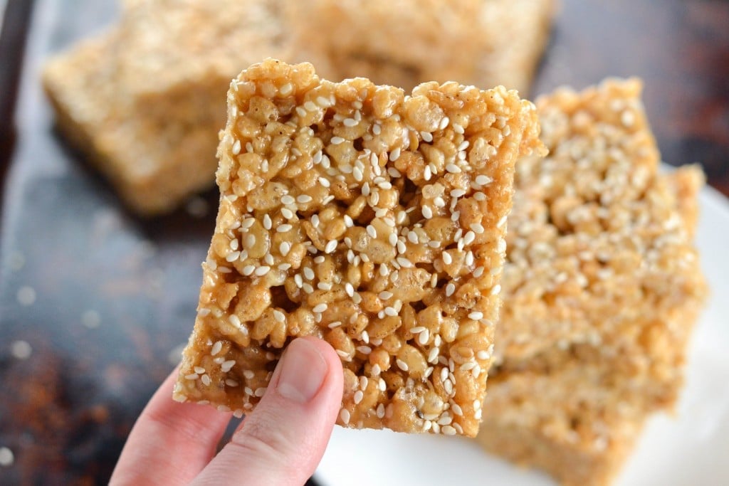 A hand holding a square tahini rice krispy treat topped with sesame seeds.