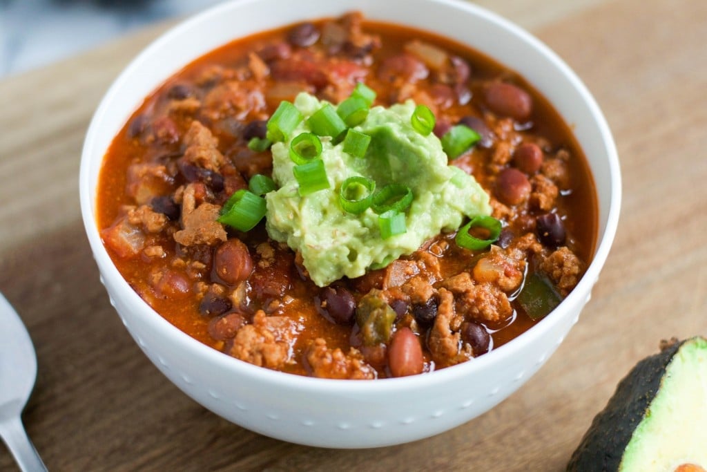 A bowl of turkey chili topped with guacamole and green onions.