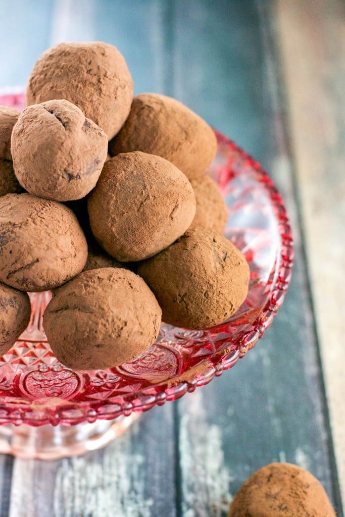 A pile of chocolate truffles rolled in cocoa powder on top of a pink cake stand.