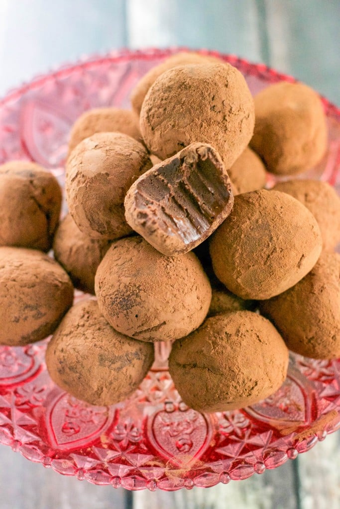 A pile of Vegan Chocolate Truffles on a pink cake stand with a bite taken out of one of the truffles.