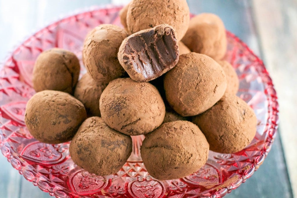 A pink cake stand with a pile of vegan chocolate truffles with a bite taken out of the top truffle.