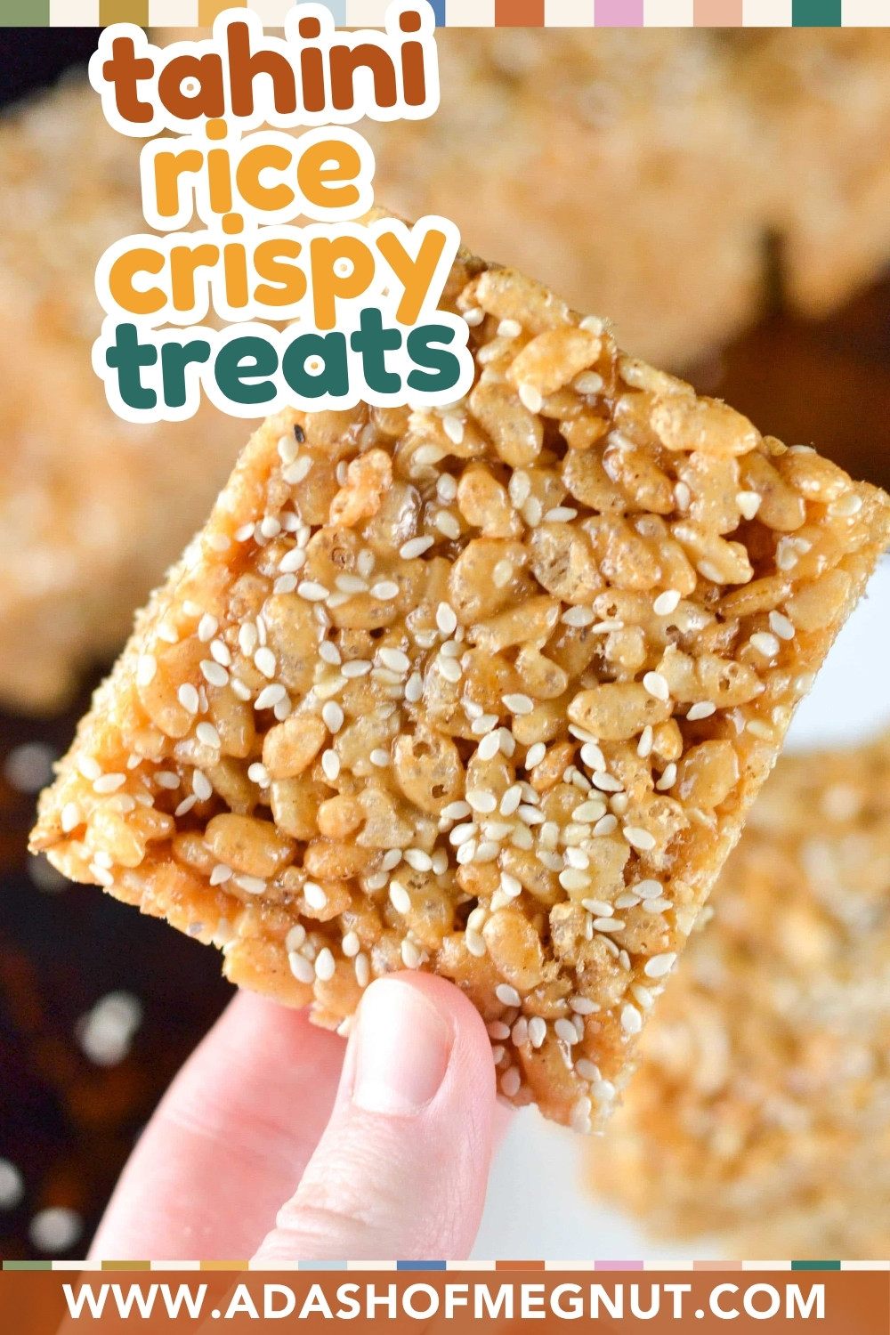 A hand holds a square tahini brown rice crispy treat topped with sesame seeds. Text on the image reads tahini rice crispy treats and www.adashofmegnut.com. The background displays more crispy treats.