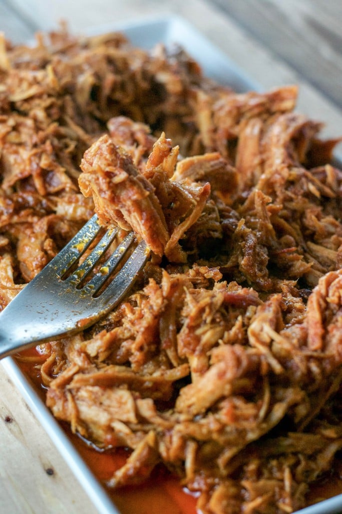 A plate of crockpot shredded pork in bbq sauce with a fork. 
