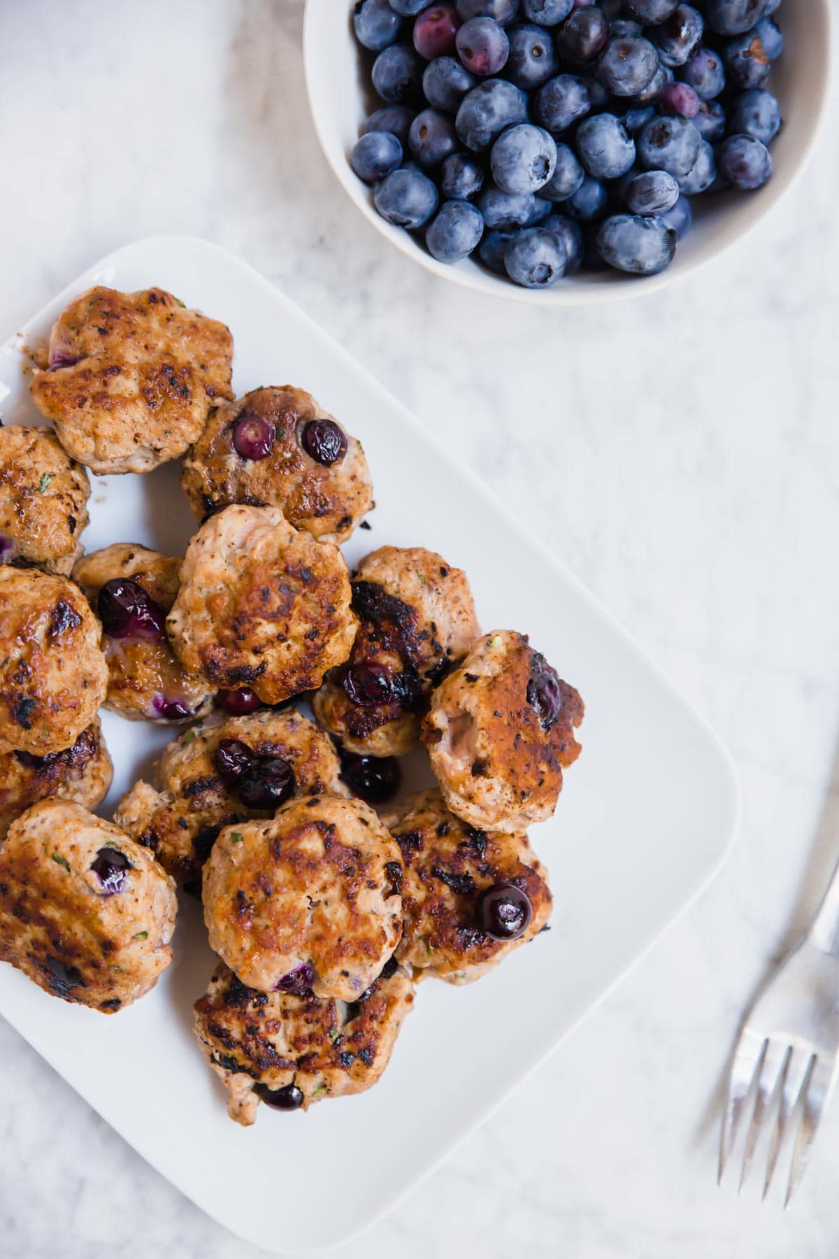 An aerial view of a plate with blueberry turkey breakfast sausage and a bowl of fresh blueberries. 