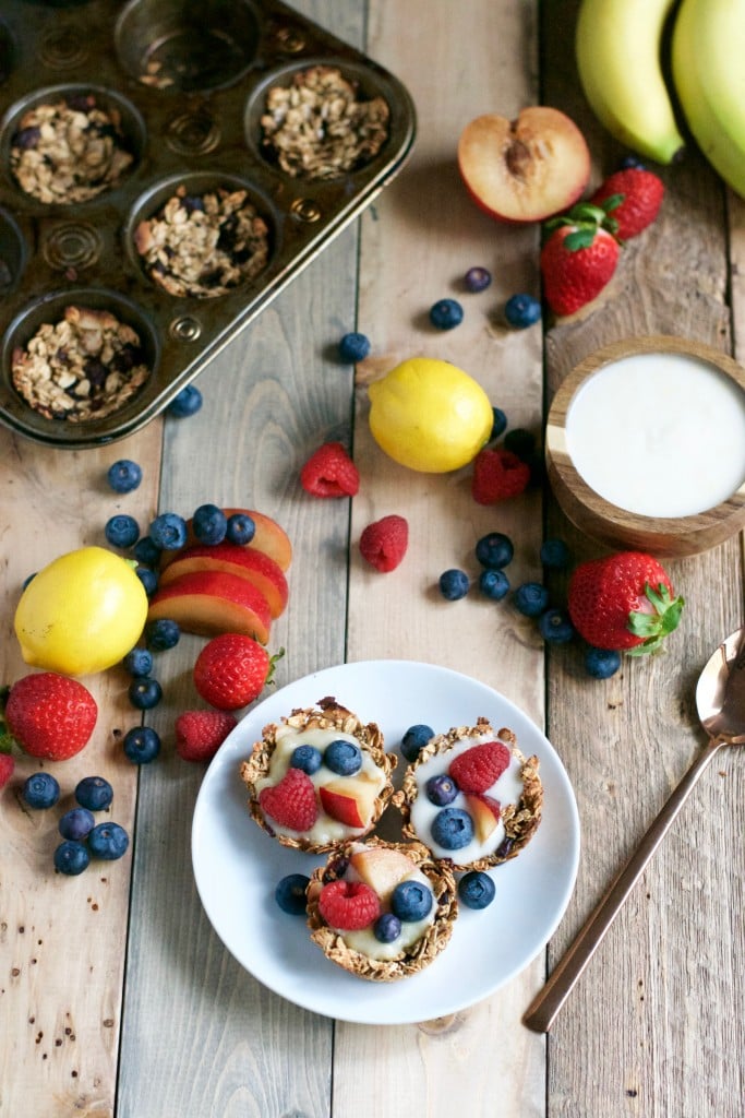 Mini granola cups on a plate filled with yogurt and fresh fruit with a muffin tin filled with granola cups in the background and a bowl of vegan yogurt.