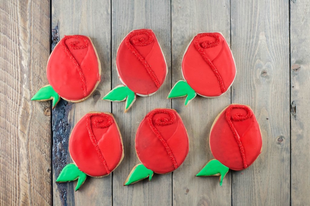 Six rose shaped sugar cookies on a wood surface.