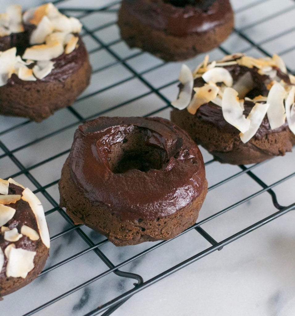 Baked vegan chocolate donuts with chocolate glaze and toasted coconut on a cooling rack. 