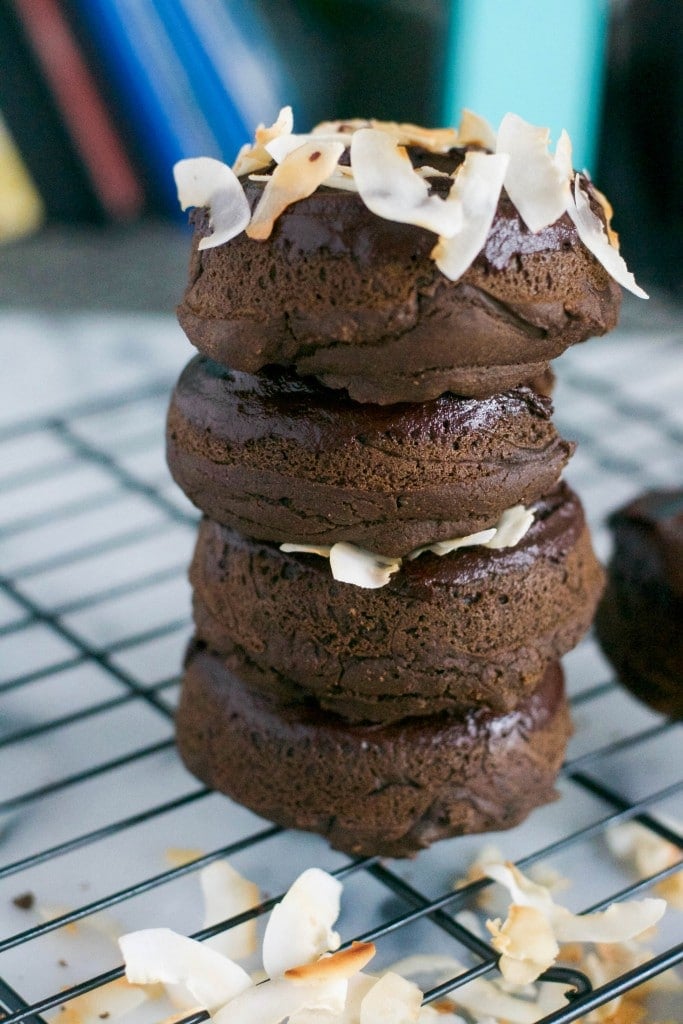 A stack of four chocolate donuts topped with toasted coconut chips on top of a cooling rack. 