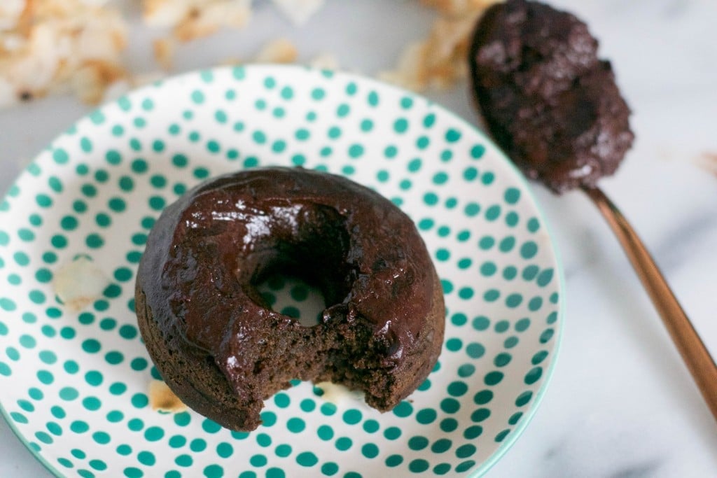 A vegan chocolate donut on a polka dot green plate with a spoon of chocolate frosting next to it.