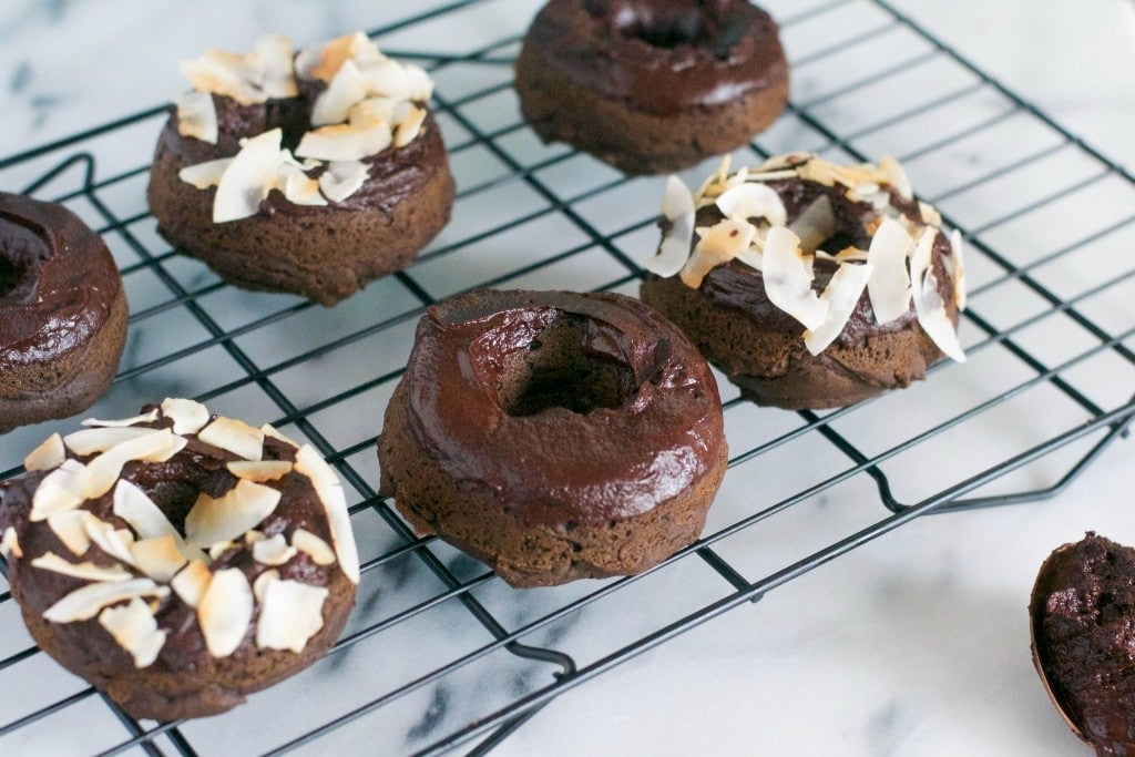 Six chocolate donuts on a cooling rack with some topped with toasted coconut chips.