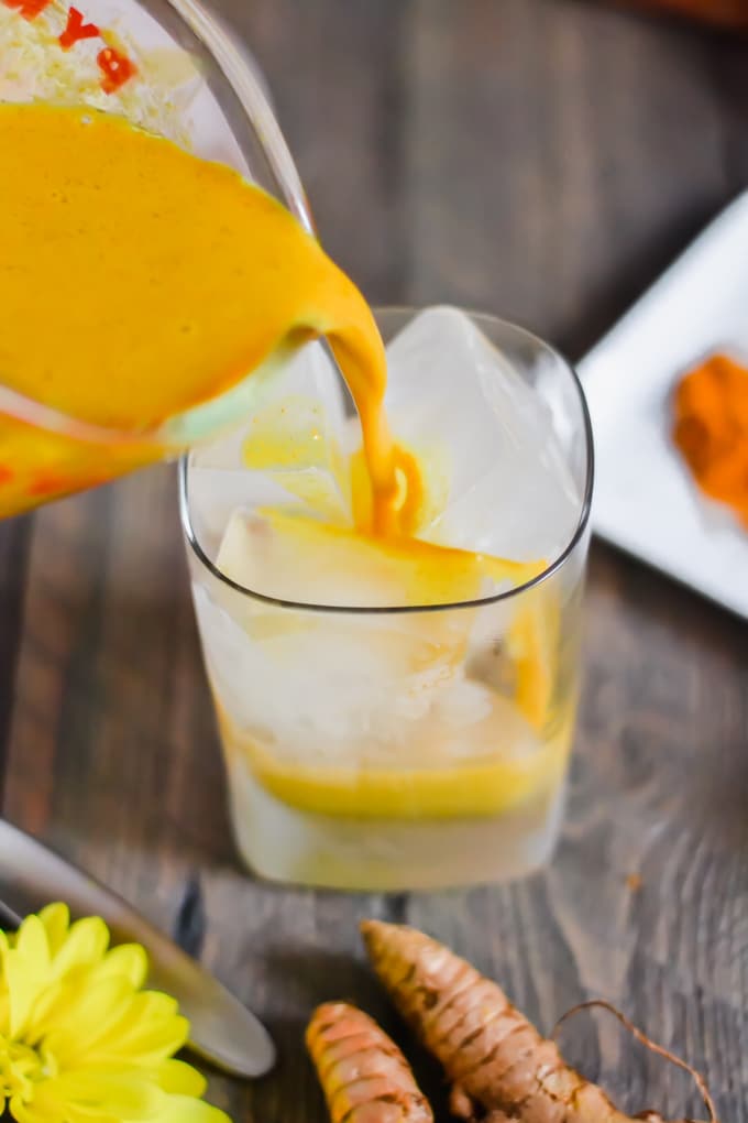 A measuring cup pouring golden milk into a glass of ice.