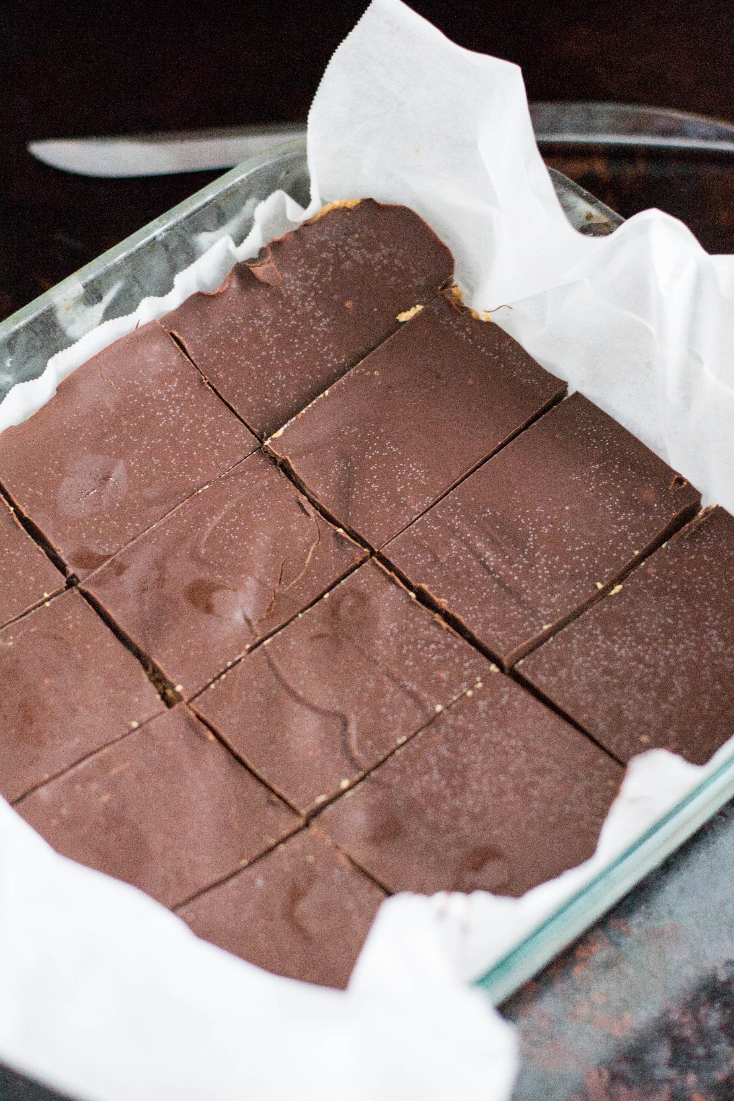 A  baking dish lined with parchment paper containing chocolate peanut butter bars that have been sliced into rectangles.