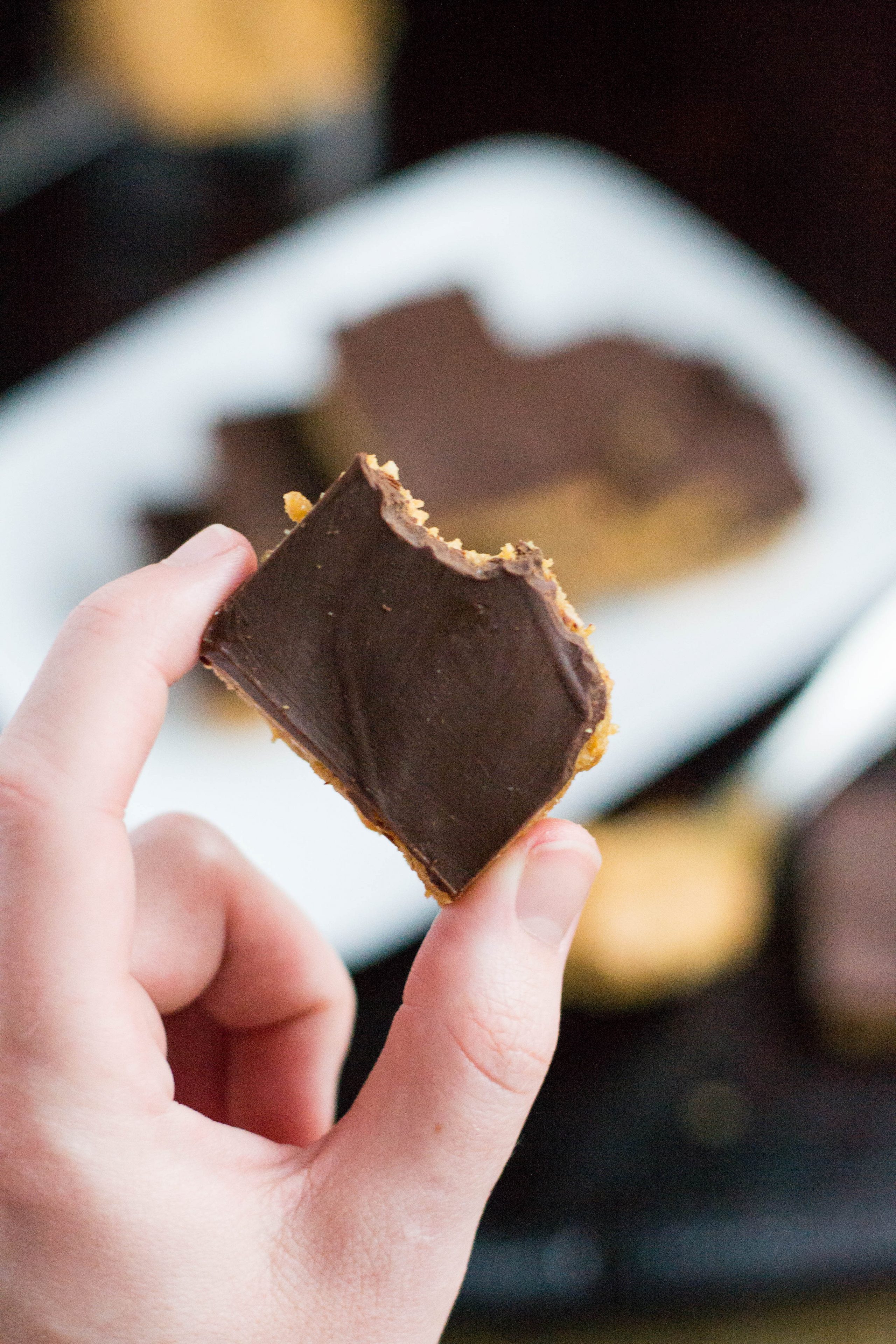 A hand holding a chocolate peanut butter bar that has a bite taken out of it.