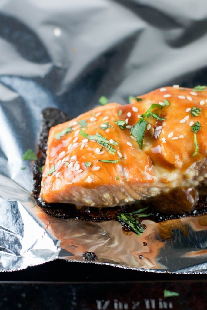 A portion of teriyaki salmon topped with parsley and sesame seeds on top of aluminum foil. 