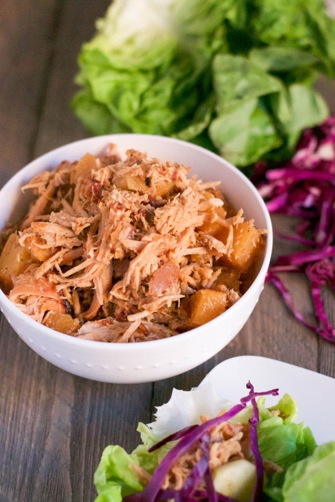 A bowl of slow cooker shredded pork with lettuce and red cabbage in the background.