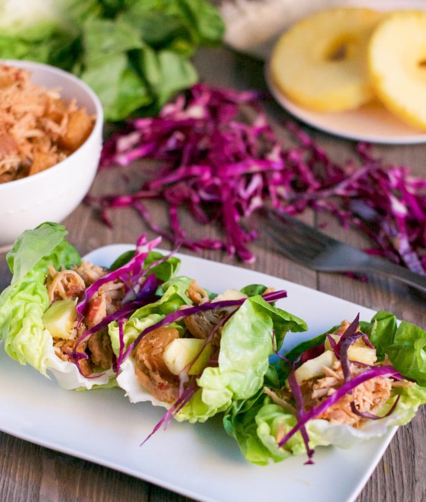 A plate with three pineapple pork lettuce wrapped topped with shredded red cabbage and avocado. 