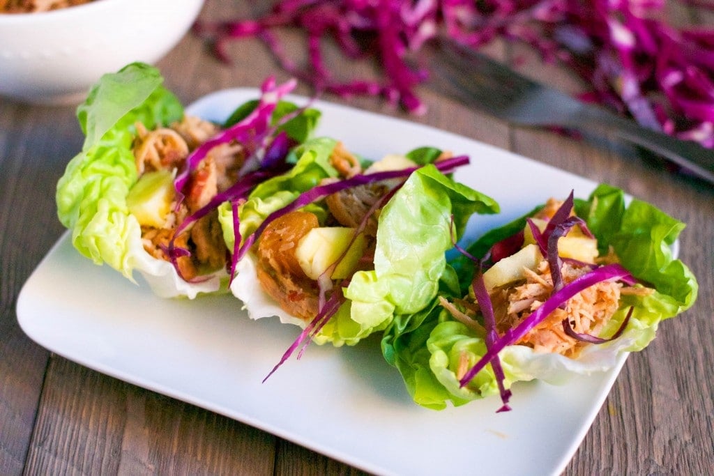 A platter with three lettuce wraps with shredded pork, pineapple and red cabbage. 