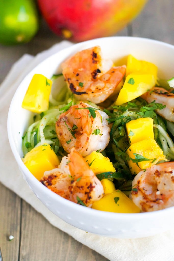 A bowl of cucumber noodles topped with shrimp, mango and cilantro. 