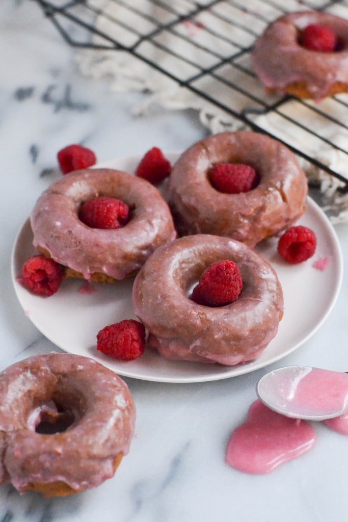 A plate with raspberry rhubarb donuts on it topped with fresh raspberries. 