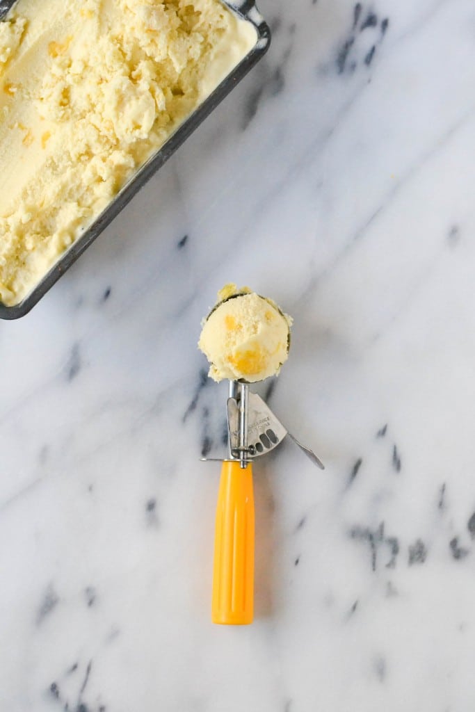 An ice cream scoop with pineapple coconut ice cream and a container of ice cream on the side.
