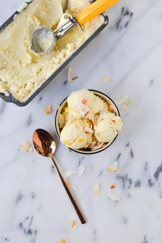 A bowl of scoops of vegan pineapple coconut ice cream with a pan of ice cream on the side.