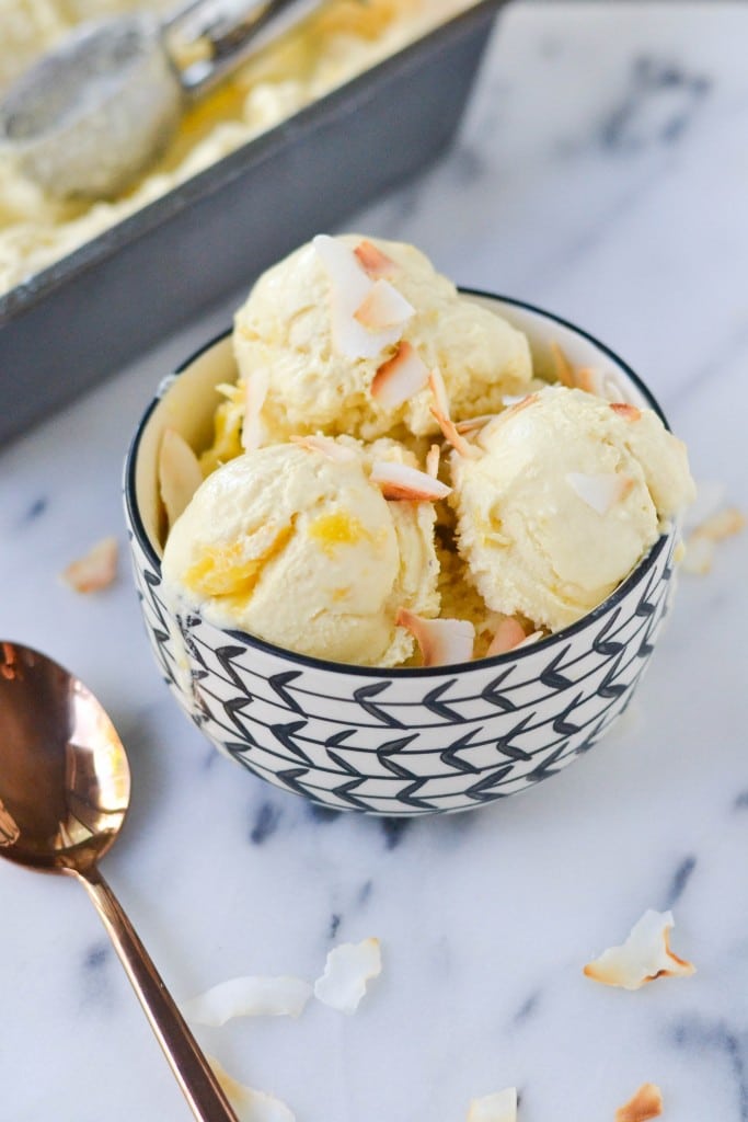 A bowl of vegan pineapple coconut ice cream topped with shredded coconut with a spoon beside it.