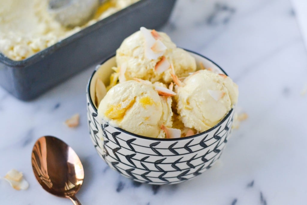 A bowl of vegan pineapple ice cream topped with toasted coconut shreds and a spoon on the side.