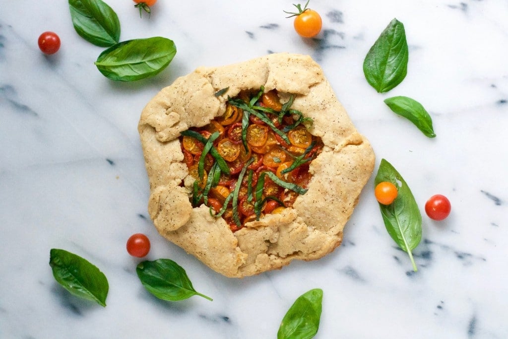 A gluten-free vegan tomato galette topped with fresh basil on a marble table. 
