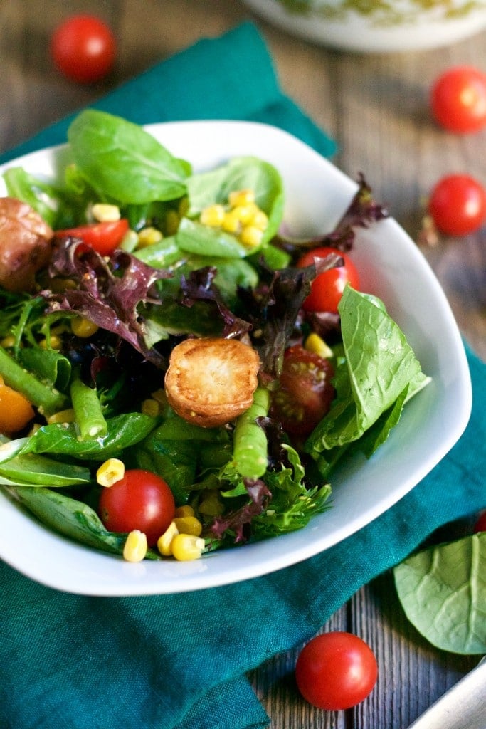 A bowl of salad with corn, cherry tomatoes, green beans, and roasted potatoes. 