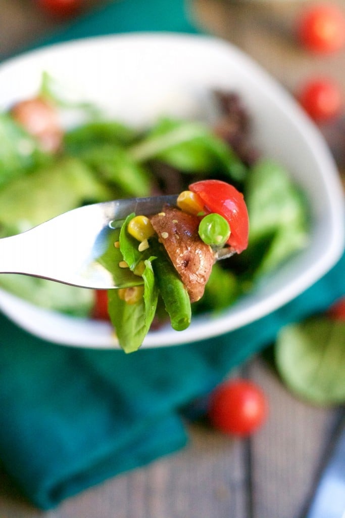 A fork full of salad with potato, tomato, green bean and corn. 