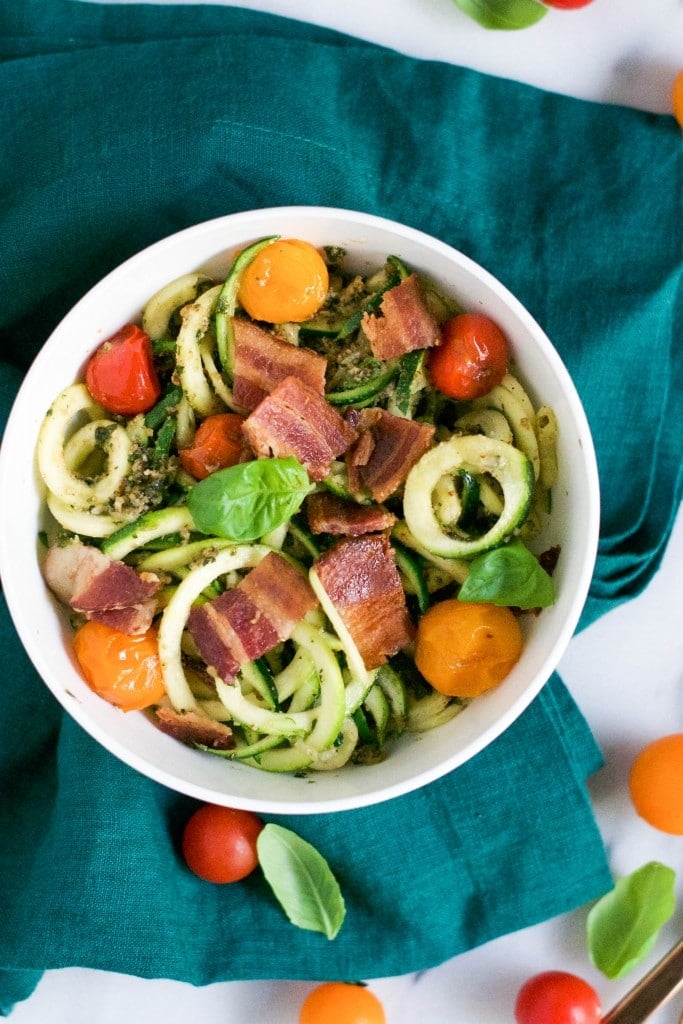 A bowl of zucchini noodles, cherry tomatoes, bacon and fresh basil.