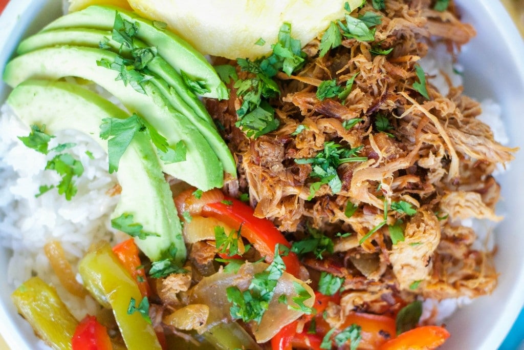 A bowl with sliced pineapple, slow cooker shredded pork, sliced avocado, bell peppers and cilantro. 