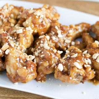 White plate of baked peanut butter chicken wings topped with chopped roasted peanuts.