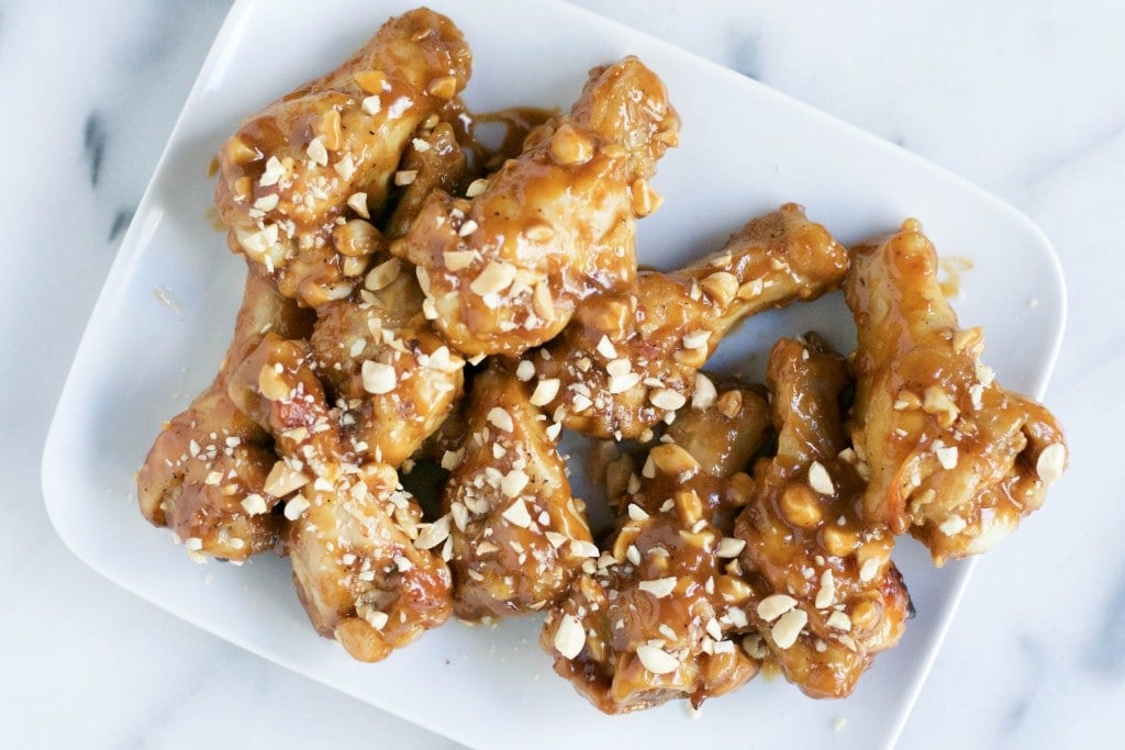 An overhead view of a platter filled with peanut butter chicken wings topped with chopped peanuts. 