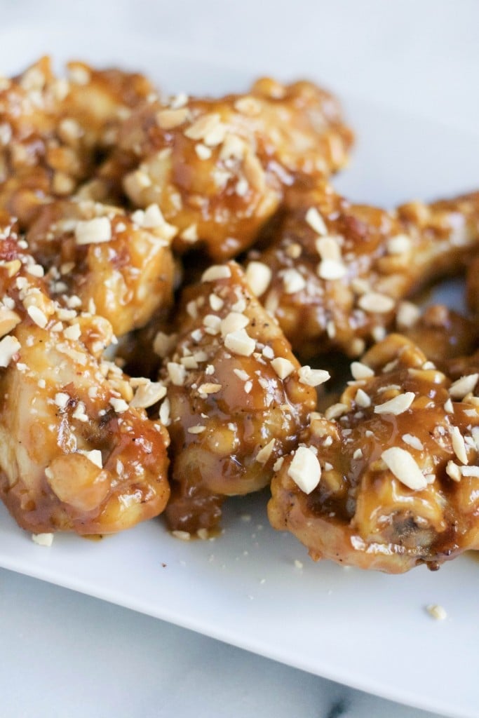 A pile of peanut butter chicken wings with chopped peanuts on top.