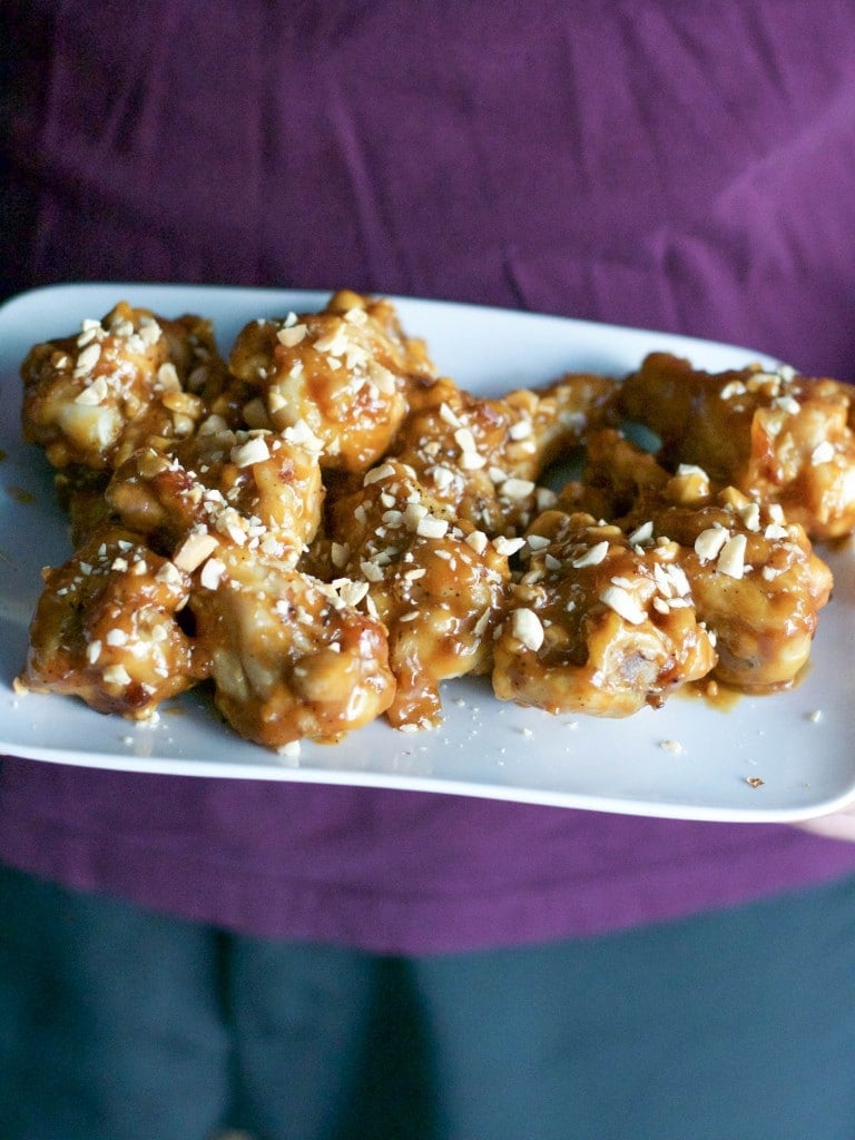 A man holding a plate full of peanut butter chicken wings topped with chopped peanuts. 